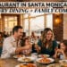 A multi-generational family enjoys a meal at an upscale restaurant in Santa Monica, with a view of the Santa Monica Pier and beach at sunset.