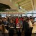 Large crowd of people waiting in line at a busy buffet with salad and hot food options on a cruise ship.