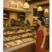 Woman in a rust-colored dress standing at the pastry counter inside Sea Beans café at Terranea Resort, with a display of fresh baked goods.