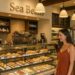 Woman in a rust-colored dress standing at the pastry counter inside Sea Beans café at Terranea Resort, with a display of fresh baked goods.