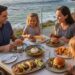 A family of four enjoys a meal outdoors on a restaurant patio ant Nelson’s overlooking a rugged coastline and the ocean at sunset.