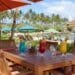 Wooden dining table with Hawaiian cocktails and beach chairs under umbrellas at The Beach House Restaurant, Turtle Bay, Oahu.