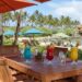 Wooden dining table with Hawaiian cocktails and beach chairs under umbrellas at The Beach House Restaurant, Turtle Bay, Oahu.