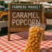 Bag of caramel popcorn displayed on a red checkered tablecloth with a farmers market sign in the background.