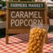 Bag of caramel popcorn displayed on a red checkered tablecloth with a farmers market sign in the background.