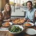 Family of four smiling at an Italian restaurant table with pizza, pasta, and salad in Los Angeles.