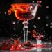 Red cocktail splashing out of an elegant glass against a dark background in a dramatic high-speed shot.