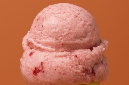 A scoop of raspberry ice cream in a waffle cone against a burnt-orange background with white text reading “Ginger’s Divine Ice Creams Review – Westside LA.”