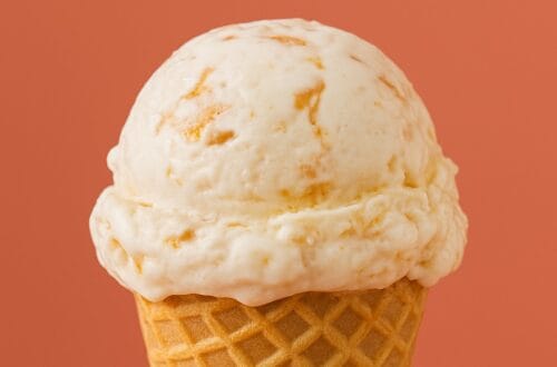 A single scoop of caramel-streaked artisan ice cream in a waffle cone against a coral background with text overlay reading “The Renaissance of Ice Cream – From Thrifty Scoops to Gourmet Creations.”