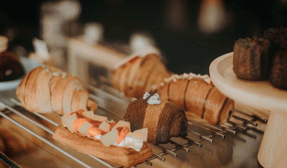 An assortment of French pastries including flaky croissants, a chocolate roulade, and a canelé displayed on a bakery cooling rack.