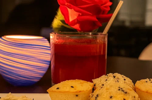 Salvadorian cheese rolls and a red Mercado Margarita with a rose garnish next to a striped blue candle on a white plate at RAYA restaurant.