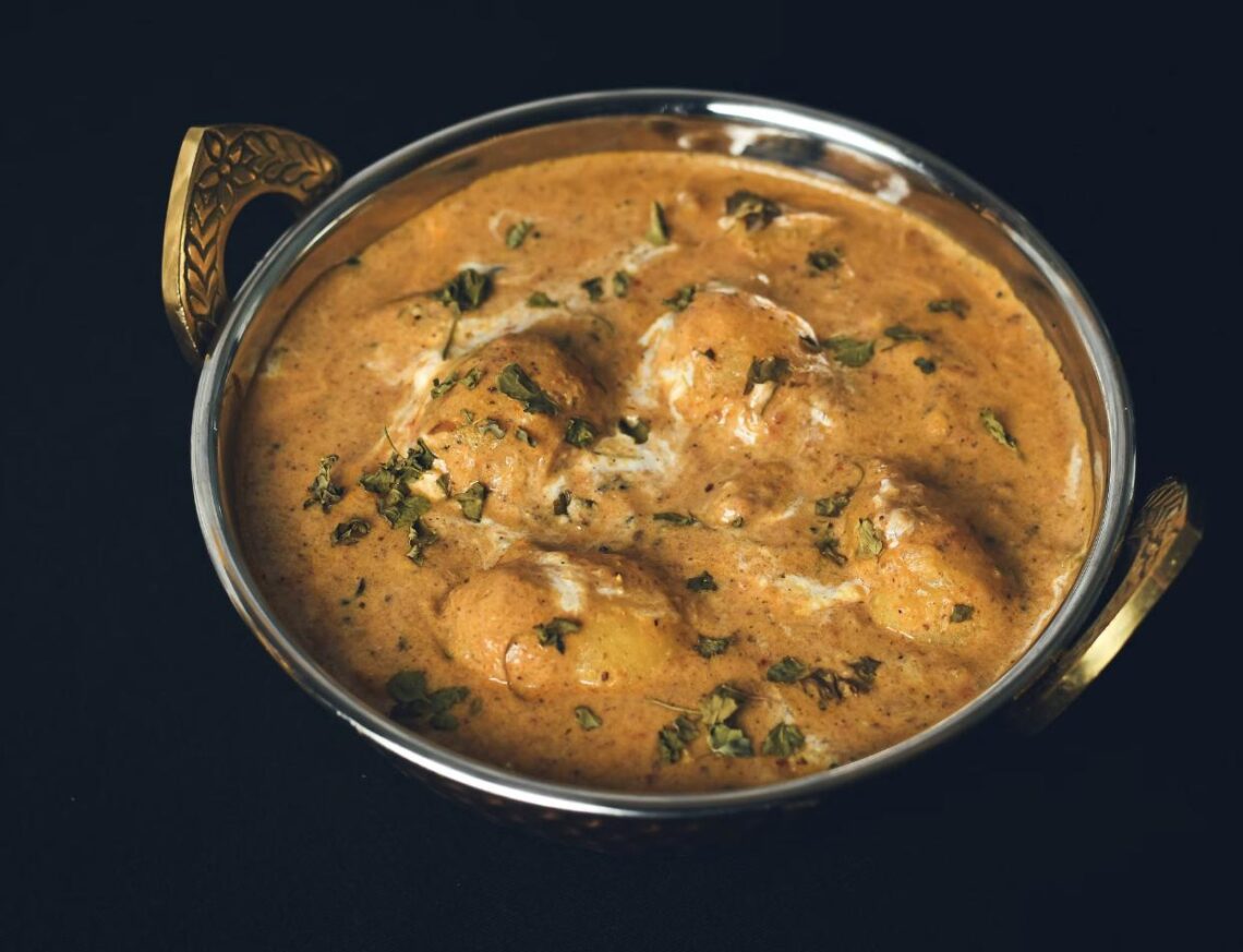 A rich, creamy regional Indian curry garnished with fresh herbs, served in a traditional brass-handled bowl.