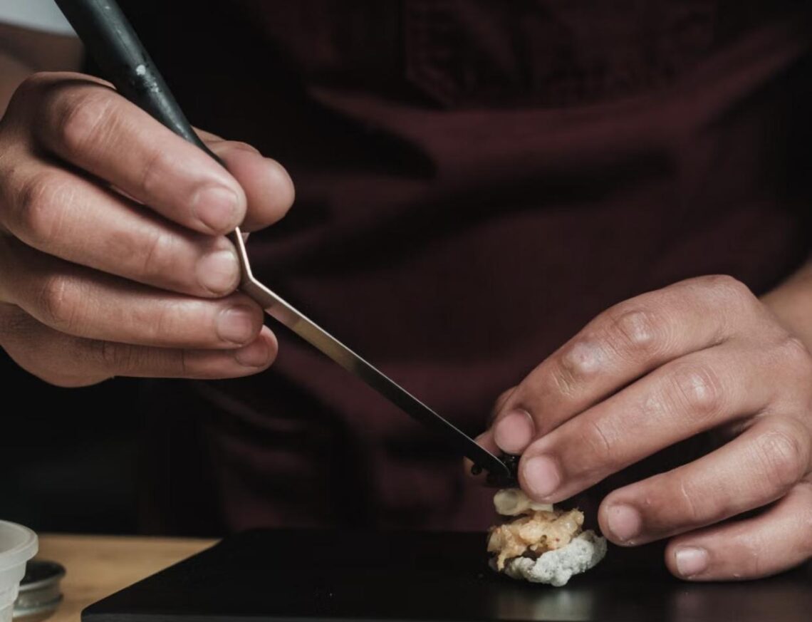A sushi chef carefully places nigiri with precision using metal tweezers during an omakase dinner.