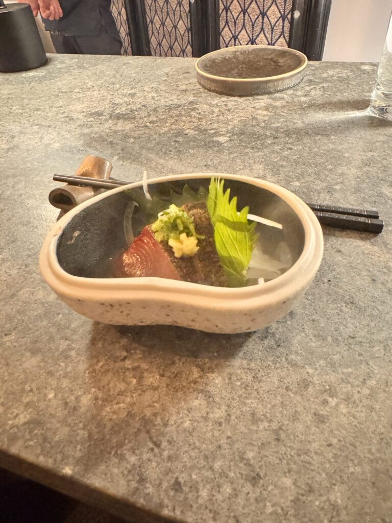 Seasonal sashimi with shiso, scallion and grated ginger in a ceramic bowl at TAIKUN