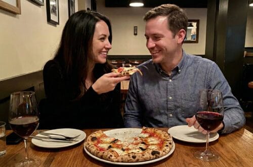 Ginger Graham feeding Brad Graham a slice of pizza in a restaurant.