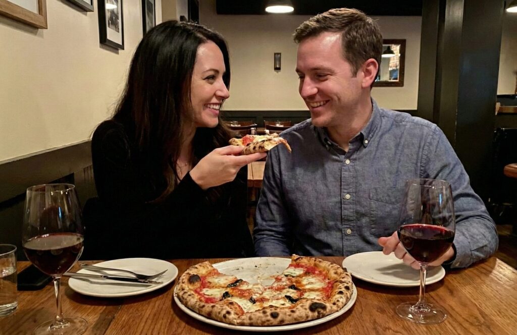 Couple laughing and sharing a playful pizza bite on a fun dating night out in Los Angeles