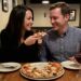 Ginger Graham feeding Brad Graham a slice of pizza in a restaurant.