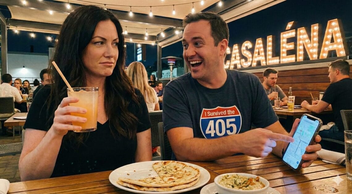 Ginger Graham (brunette woman) and Brad Graham (man) dining at Casaléna restaurant in Woodland Hills. Ginger looks skeptical holding a cocktail while Brad smiles broadly, holding a smartphone showing a map. Outdoor patio dining setting with string lights.
