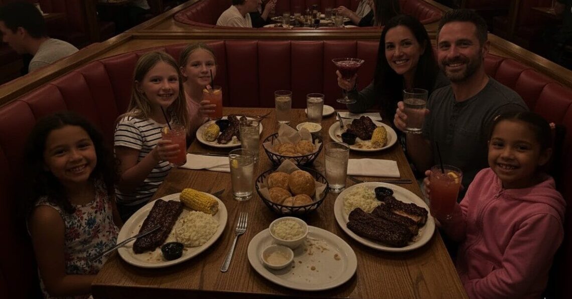 A family and their friends, two adults and four girls, happily eating ribs in a cozy, dimly lit red booth at Wood Ranch BBQ, with the mom holding a martini and kids drinking strawberry lemonade.