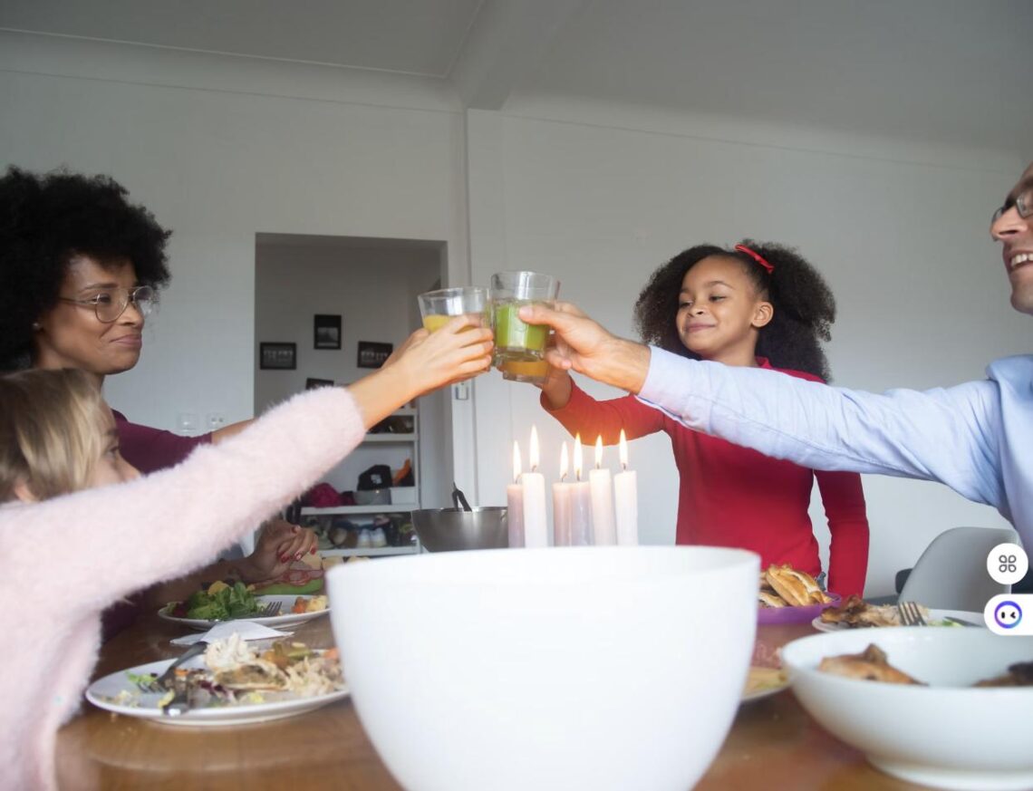 A family of four toasts with drinks over a candlelit dinner table at home.