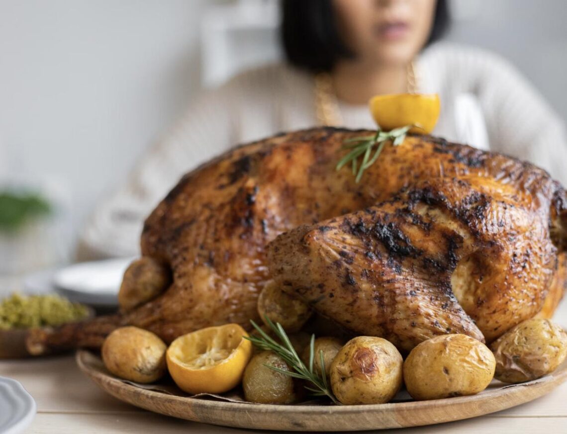 A whole roasted turkey with deep golden, crispy skin, garnished with lemon and rosemary on a platter of roasted potatoes.