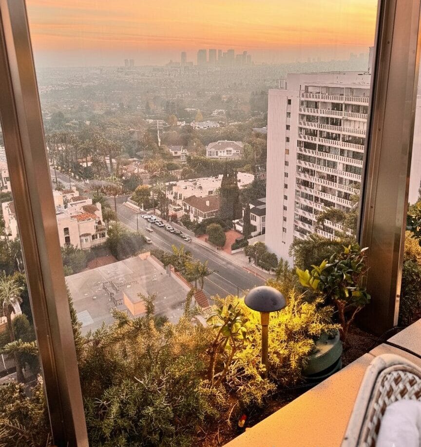 A gourmet dinner spread including Short Rib Barbacoa Nachos and a Sun and Shade cocktail on a marble table at The Roof at EDITION, overlooking a golden West Hollywood sunset.