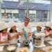 Chef and five giggling 8-year-old girls in chef hats and personalized aprons baking cookies and cupcakes in a professional kitchen at The Gourmandise School in Santa Monica.