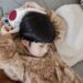 A child cuddles a stuffed animal while wrapped in a cozy plush wearable blanket on the couch.