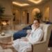 A woman in a white luxury bathrobe relaxing in a plush spa lounge with a warm drink, representing a wellness retreat at Canyon Ranch Spa in Las Vegas.