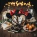 A high-quality flatlay of luxury party favors including sequined Mickey Mouse ears, artisanal candles, linen gift bags, and hardcover sketchbooks on a rustic wooden table.