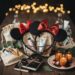A high-quality flatlay of luxury party favors including sequined Mickey Mouse ears, artisanal candles, linen gift bags, and hardcover sketchbooks on a rustic wooden table.