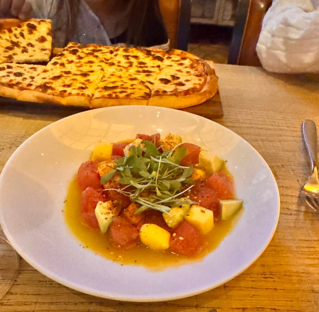A white bowl of tuna poke with mango and avocado in a citrus broth, served alongside a cheesy flatbread at CRUSH restaurant in Las Vegas.