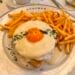 A gourmet Croque Madame topped with a fried egg and Mornay sauce, served with golden French fries on a signature Bouchon Bakery plate next to a cup of espresso.