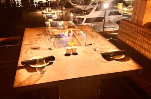 Outdoor fire-pit dining table at Cast & Plow in the Ritz-Carlton Marina del Rey overlooking luxury yachts at night.