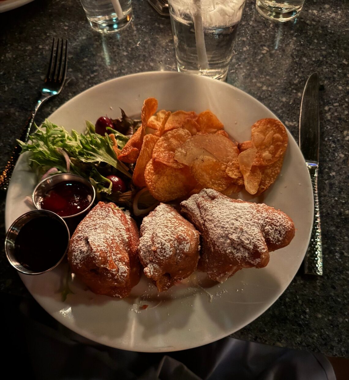 A close-up of the famous deep-fried Monte Cristo sandwich at Blue Bayou Restaurant in Disneyland, served with house-made chips, a side salad, and berry dipping sauce under moody lagoon lighting.