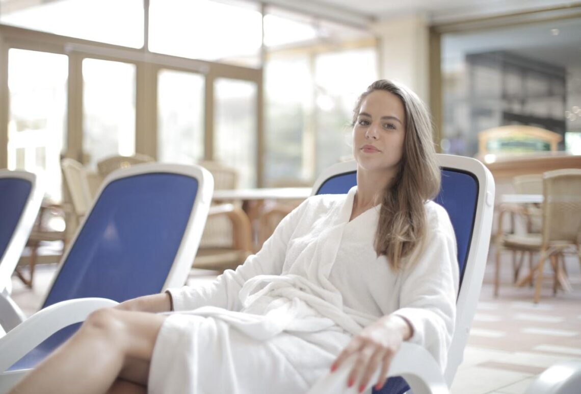 A woman in a white spa robe relaxes on a lounge chair at a wellness retreat.