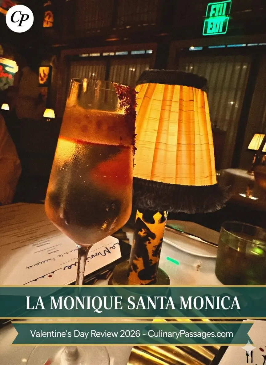 A sophisticated dining scene at La Monique in Santa Monica featuring a clarified cocktail with a garnet rim next to a vintage-style pleated lampshade and a prix-fixe Valentine's Day menu on a white tablecloth.