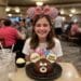 An 11-year-old girl named Madeline wearing pink "Birthday Girl" Mickey ears, smiling behind a chocolate Mickey Mouse celebration cake at a Disneyland restaurant.