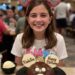 An 11-year-old girl named Madeline wearing pink "Birthday Girl" Mickey ears, smiling behind a chocolate Mickey Mouse celebration cake at a Disneyland restaurant.