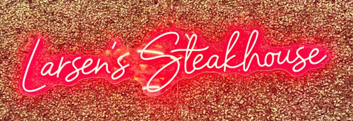 A glowing red neon sign that reads "Larsen’s Steakhouse" mounted on a textured, gold-glittered accent wall at the Woodland Hills location.