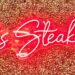 A glowing red neon sign that reads "Larsen’s Steakhouse" mounted on a textured, gold-glittered accent wall at the Woodland Hills location.