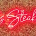 A glowing red neon sign that reads "Larsen’s Steakhouse" mounted on a textured, gold-glittered accent wall at the Woodland Hills location.