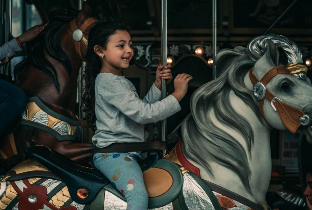 A young girl smiles while riding a carousel horse at an amusement park.