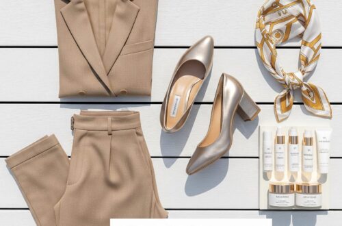 A high-end flat lay of luxury cruise essentials including tan linen trousers, a gold metallic block heel, a silk designer headscarf, and high-end travel skincare on a white wooden deck.