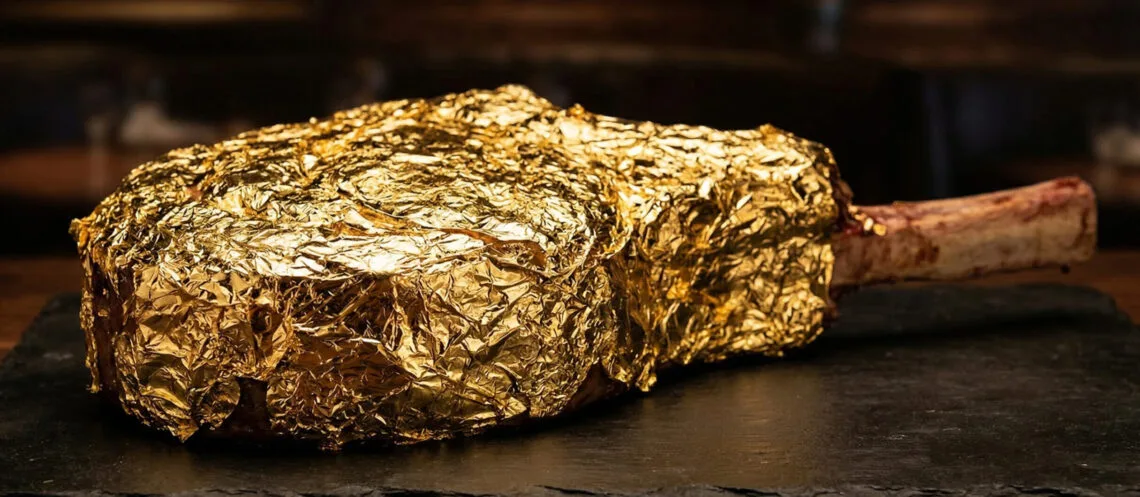 Macro photo of a glistening $1,000 Tomahawk steak covered in edible 24k gold leaf in a moody LA restaurant setting.