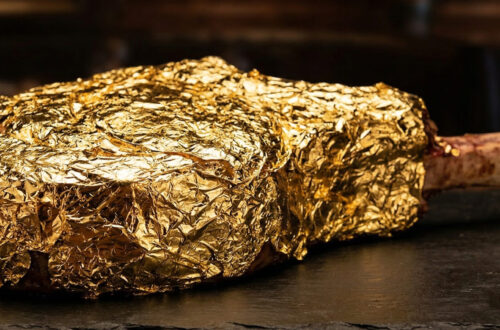 Macro photo of a glistening $1,000 Tomahawk steak covered in edible 24k gold leaf in a moody LA restaurant setting.