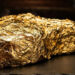 Macro photo of a glistening $1,000 Tomahawk steak covered in edible 24k gold leaf in a moody LA restaurant setting.