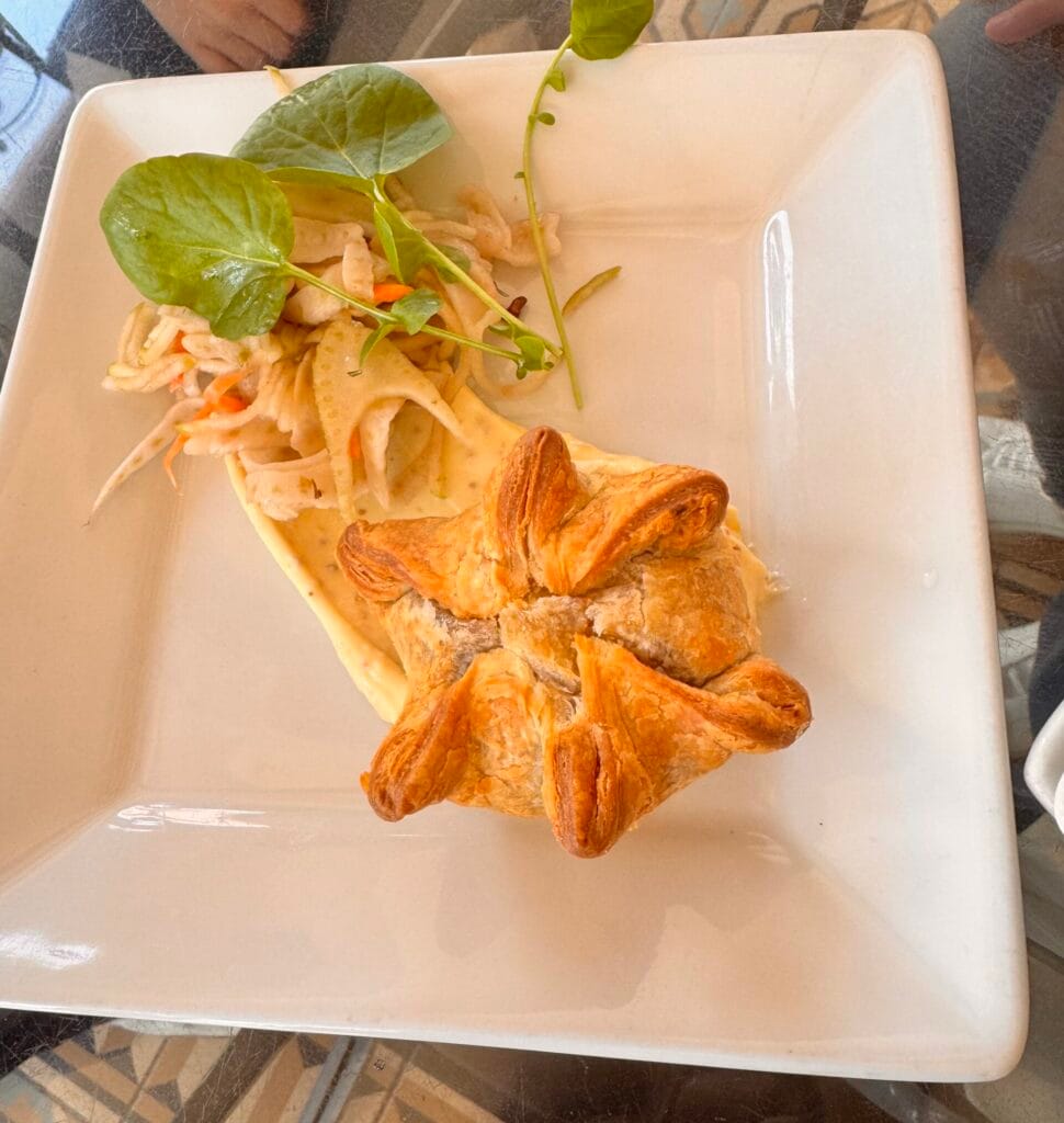 A star-shaped baked brie wrapped in golden puff pastry, served with a side of fennel apple slaw and garnished with watercress on a white square plate at Perch LA.
