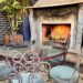 A cozy outdoor patio at Perch LA featuring a roaring stone fireplace and an ornate wrought-iron table and chairs on geometric patterned tile.