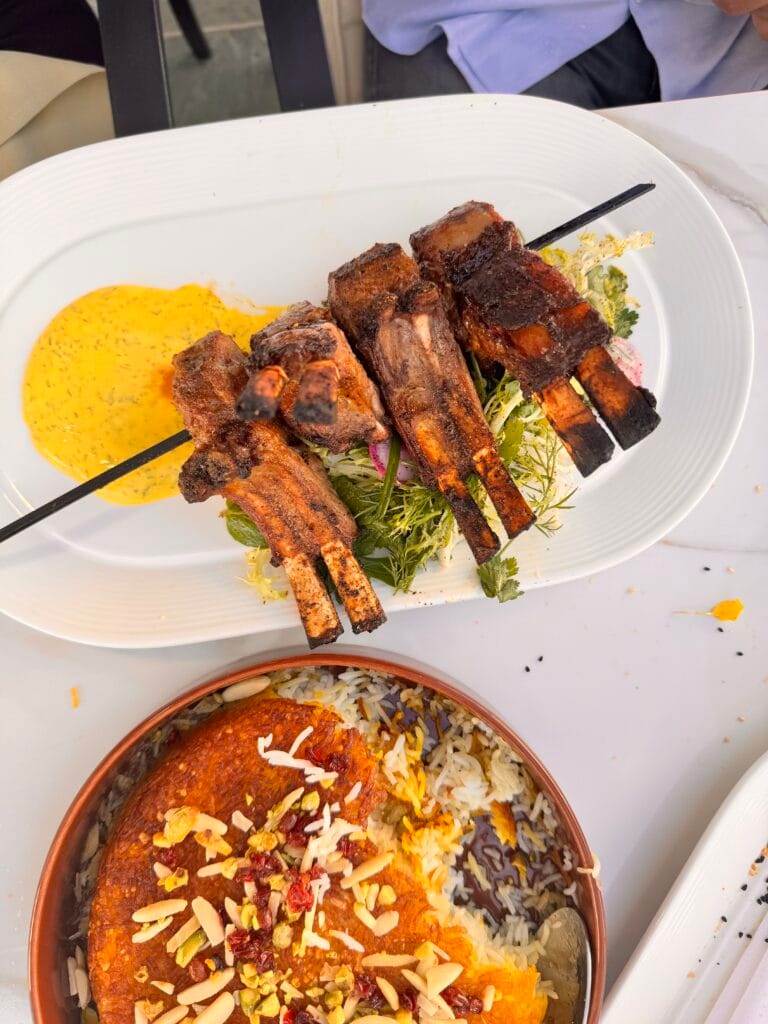 Overhead view of Saffron Lamb Chops on a skewer served with yellow saffron crema and a bowl of Smoked Saffron Tahdig topped with slivered almonds, pistachios, and barberries at Perse Restaurant.